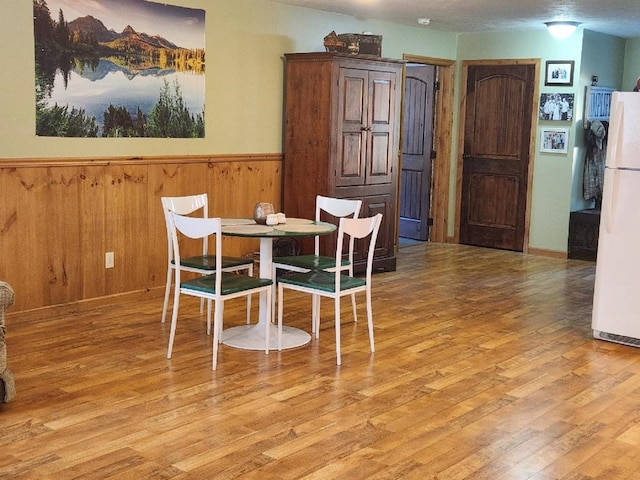 dining area featuring light wood-style floors, a wainscoted wall, and wooden walls