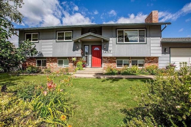 raised ranch with brick siding, a chimney, an attached garage, and a front lawn