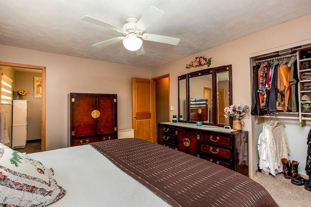 carpeted bedroom featuring a textured ceiling, white fridge, ceiling fan, and a closet