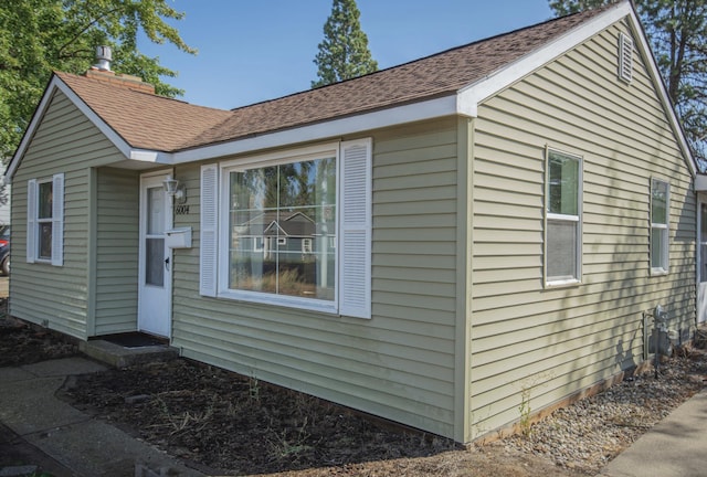 view of home's exterior with roof with shingles and a chimney