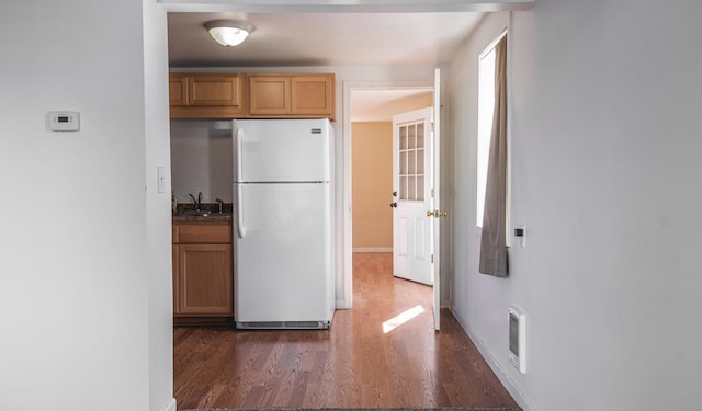 kitchen with dark wood-style floors, visible vents, freestanding refrigerator, a sink, and baseboards