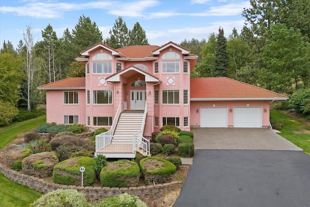 view of front of house with an attached garage, a tile roof, concrete driveway, stairway, and stucco siding