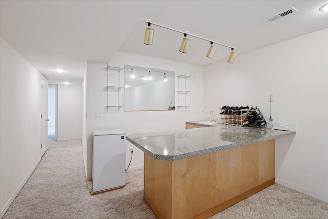 kitchen with light carpet, track lighting, kitchen peninsula, light stone countertops, and white refrigerator