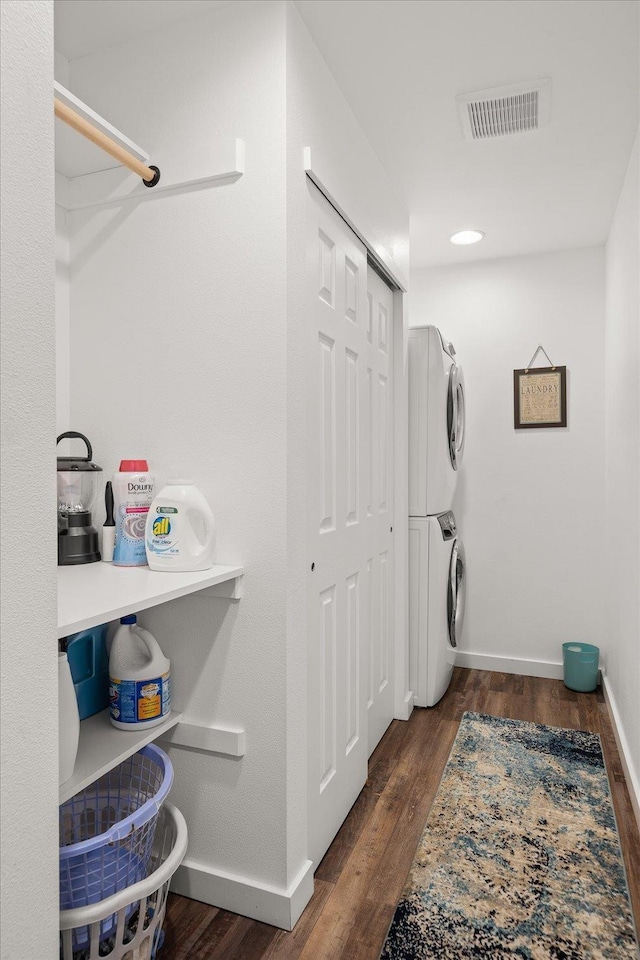 washroom with stacked washer and dryer, laundry area, baseboards, visible vents, and wood finished floors