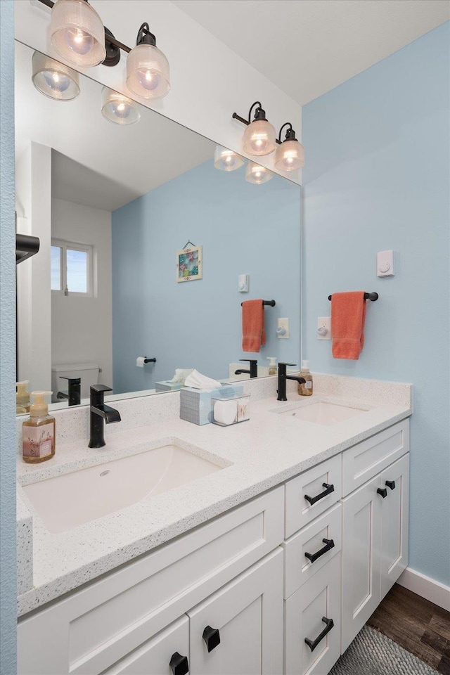 bathroom with wood finished floors, a sink, baseboards, and double vanity