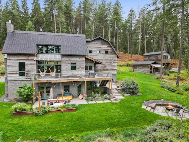 back of house featuring a deck, a patio, a fire pit, a lawn, and a chimney