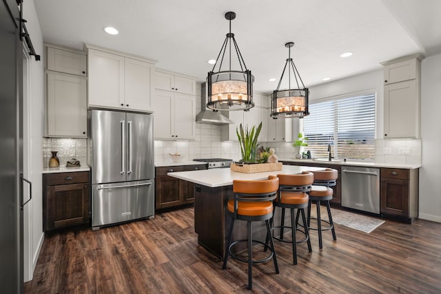 kitchen featuring dark hardwood / wood-style flooring, a center island, stainless steel appliances, a chandelier, and wall chimney range hood