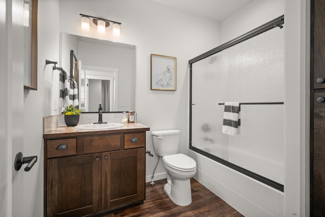 full bathroom with toilet, hardwood / wood-style floors, vanity, decorative backsplash, and bath / shower combo with glass door