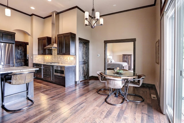 kitchen with dark brown cabinetry, tasteful backsplash, dark wood finished floors, wall chimney exhaust hood, and stainless steel appliances