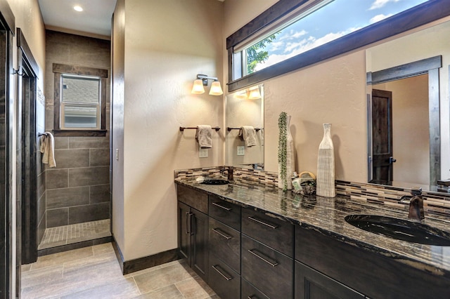 bathroom with double vanity, tiled shower, a sink, and baseboards