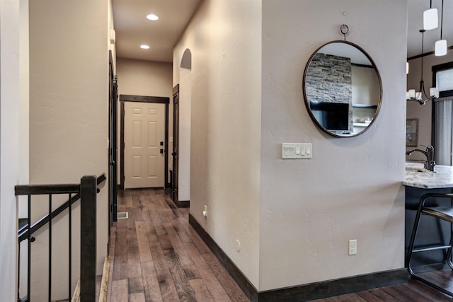 hallway with baseboards, dark wood finished floors, a sink, and recessed lighting