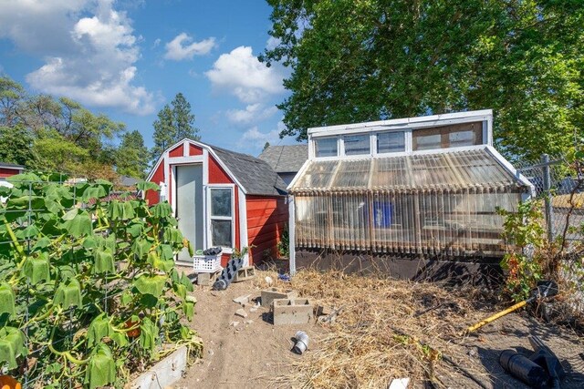 rear view of property with a shingled roof, fence, a greenhouse, and an outdoor structure