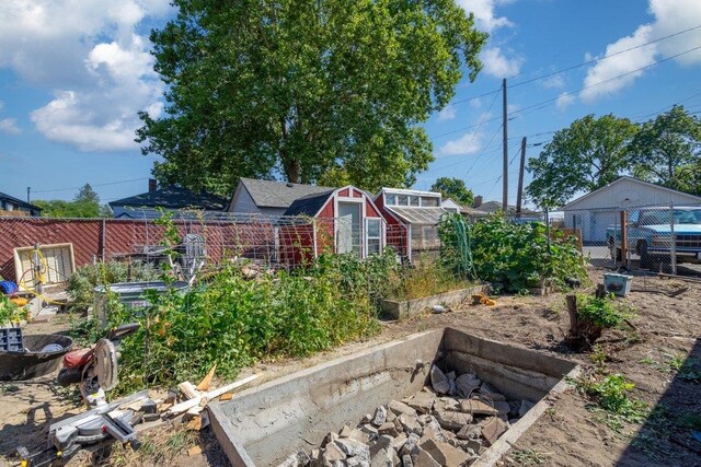 view of yard featuring a greenhouse, an outdoor structure, a vegetable garden, and fence