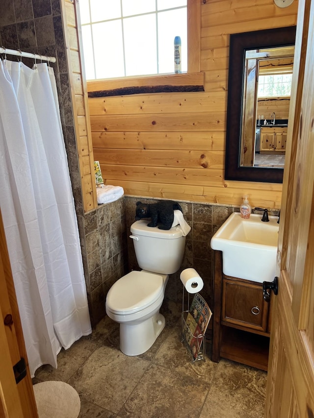 bathroom featuring a shower with curtain, wooden walls, vanity, and toilet