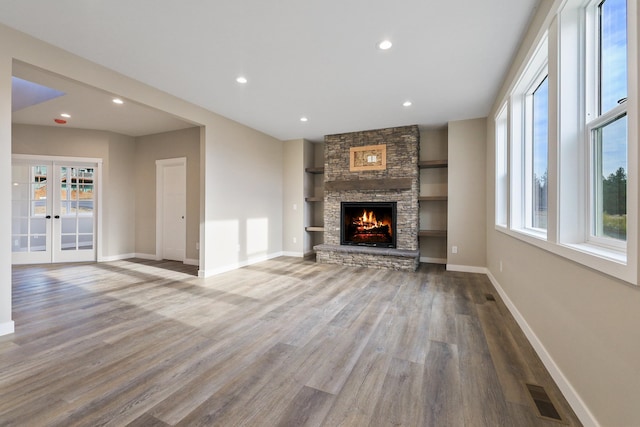 unfurnished living room featuring hardwood / wood-style floors, a stone fireplace, french doors, and plenty of natural light