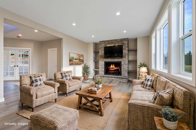 living room featuring french doors, a stone fireplace, light hardwood / wood-style floors, and plenty of natural light