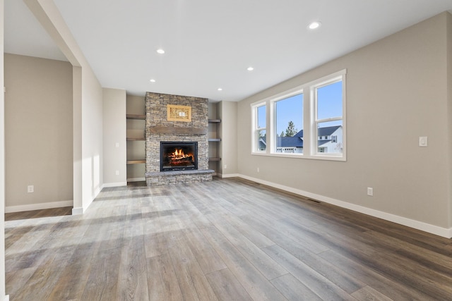 unfurnished living room featuring a stone fireplace, light hardwood / wood-style flooring, and built in shelves