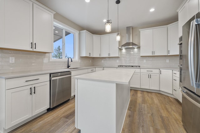 kitchen featuring wall chimney exhaust hood, appliances with stainless steel finishes, a kitchen island, and white cabinets