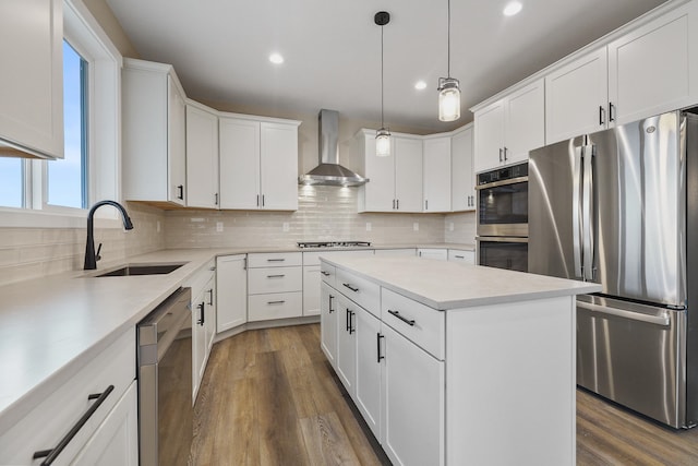 kitchen with wall chimney range hood, appliances with stainless steel finishes, sink, a center island, and white cabinetry