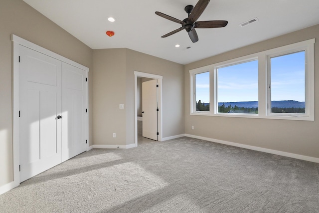 unfurnished bedroom featuring light carpet, a mountain view, and ceiling fan