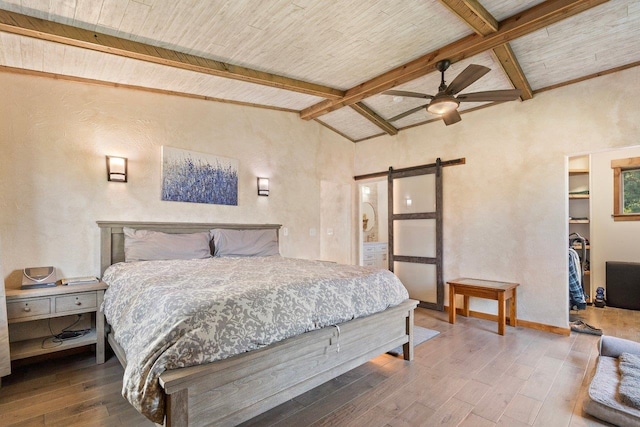 bedroom with a spacious closet, hardwood / wood-style flooring, a barn door, ceiling fan, and vaulted ceiling with beams