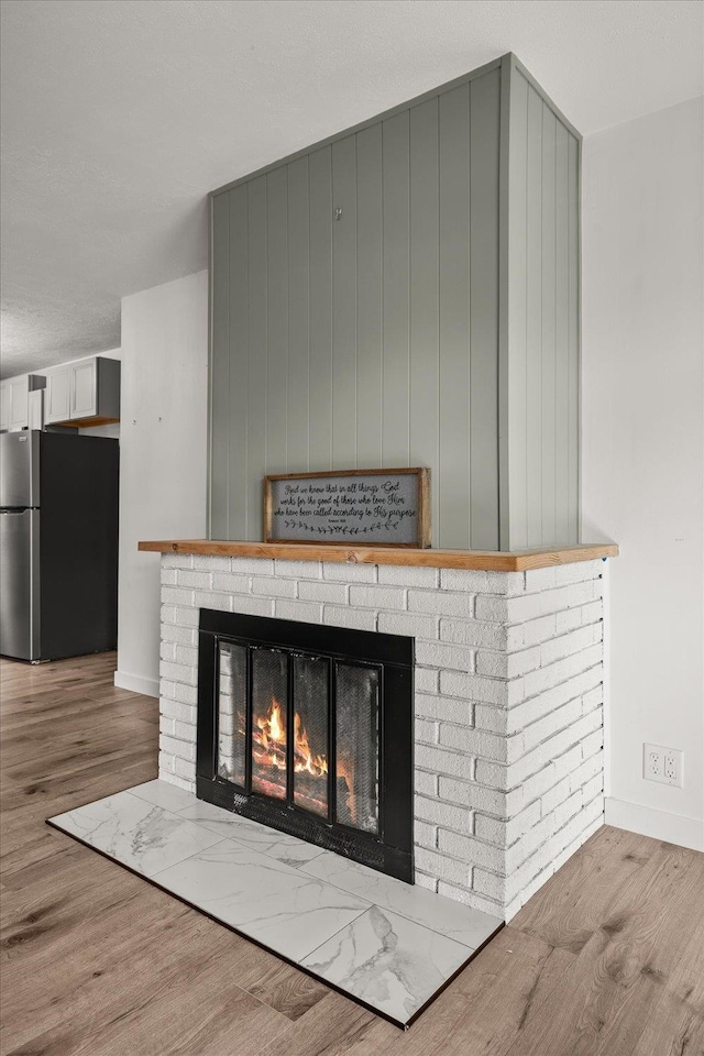 room details with hardwood / wood-style flooring, stainless steel refrigerator, and a brick fireplace