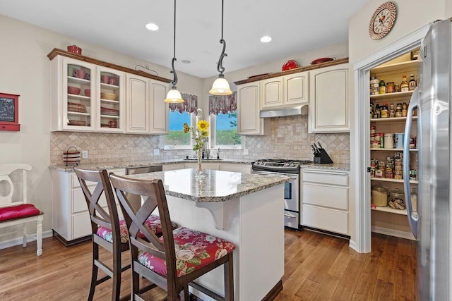 kitchen with light hardwood / wood-style flooring, backsplash, a center island, hanging light fixtures, and appliances with stainless steel finishes