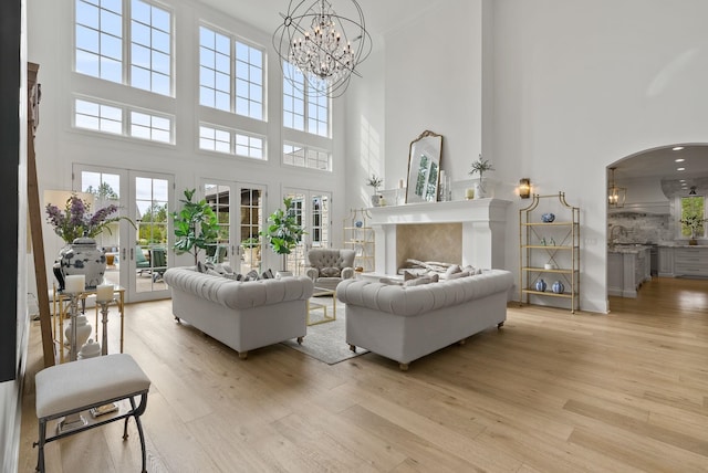 living room featuring a high end fireplace, light hardwood / wood-style flooring, an inviting chandelier, a towering ceiling, and french doors