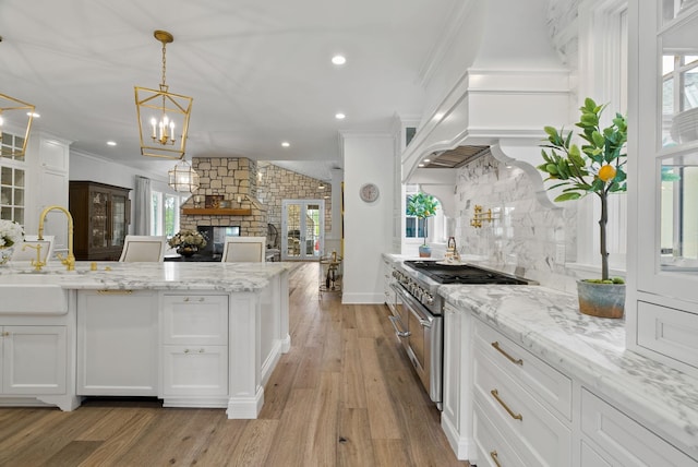 kitchen featuring white cabinets, a fireplace, high end stainless steel range, light hardwood / wood-style flooring, and light stone counters