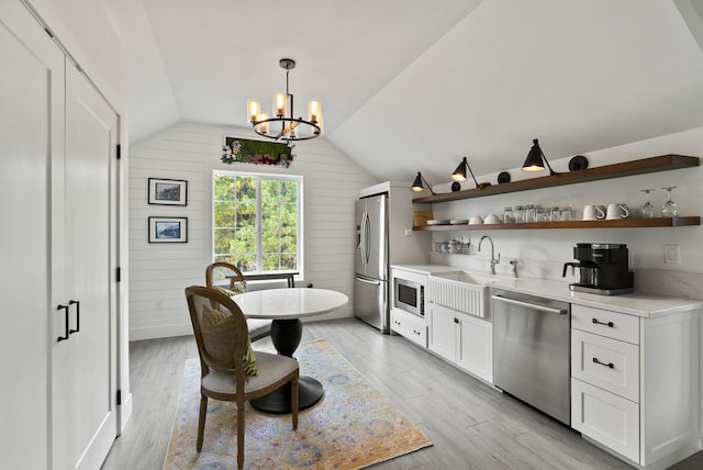 interior space featuring vaulted ceiling, appliances with stainless steel finishes, light hardwood / wood-style floors, white cabinetry, and wooden walls