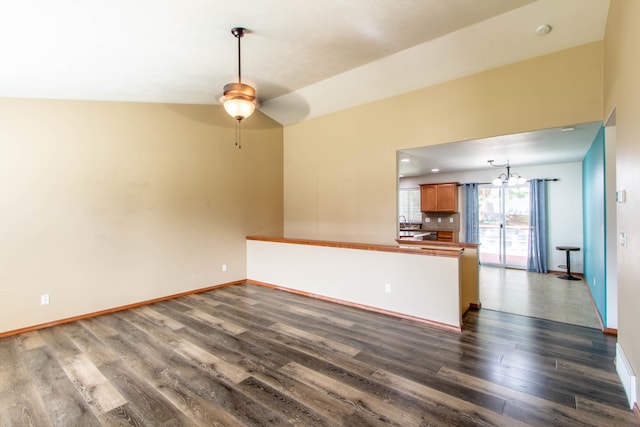 empty room with ceiling fan with notable chandelier, dark hardwood / wood-style flooring, and lofted ceiling