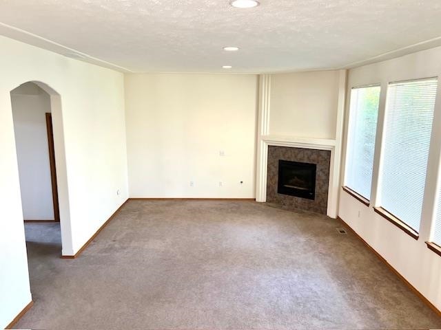 unfurnished living room featuring dark carpet, a textured ceiling, and a tile fireplace