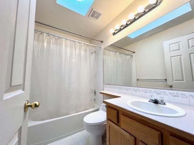 full bathroom with vanity, a skylight, shower / tub combo with curtain, toilet, and tile patterned floors