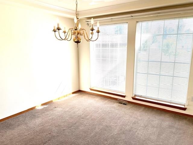 carpeted spare room featuring ornamental molding and an inviting chandelier