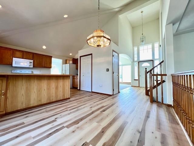 kitchen with pendant lighting, a notable chandelier, light hardwood / wood-style flooring, high vaulted ceiling, and white appliances