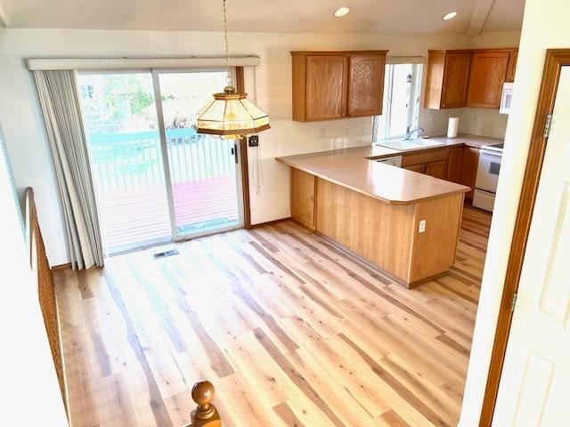 kitchen with pendant lighting, sink, kitchen peninsula, white appliances, and light wood-type flooring