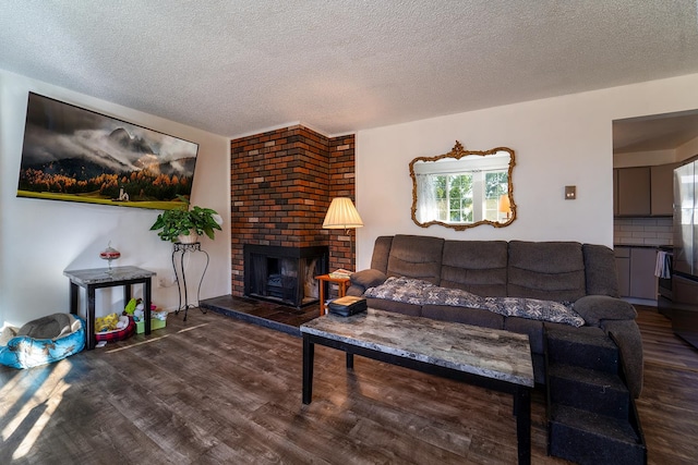 living room with a textured ceiling, dark wood-type flooring, and a brick fireplace