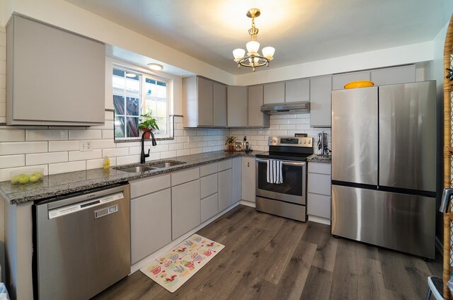 kitchen with sink, a chandelier, stainless steel appliances, dark hardwood / wood-style floors, and dark stone counters