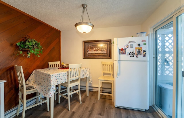 dining area with wooden walls, a textured ceiling, and dark hardwood / wood-style flooring