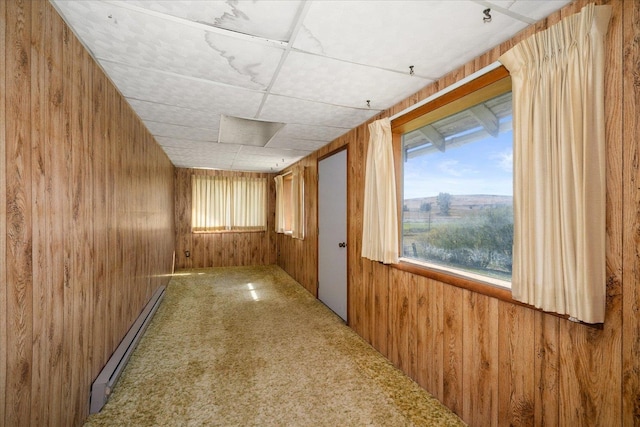 hall featuring a paneled ceiling, carpet flooring, wood walls, and a baseboard heating unit