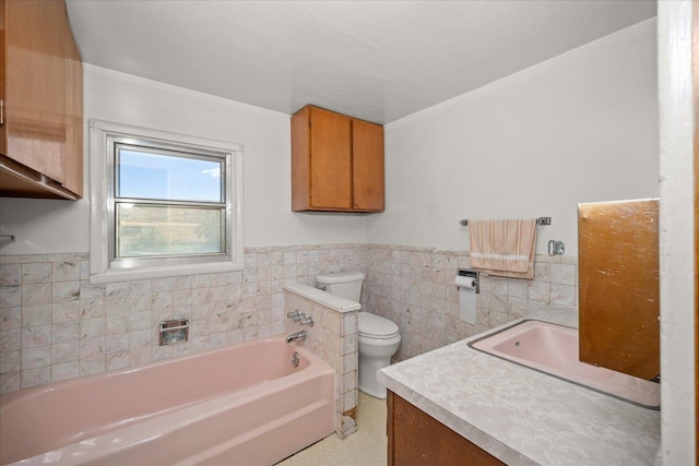 bathroom with vanity, a bathtub, toilet, and tile walls