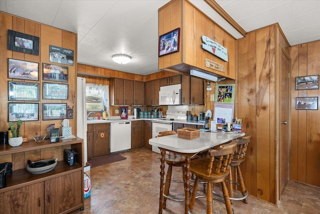 kitchen with kitchen peninsula, wood walls, sink, and white appliances