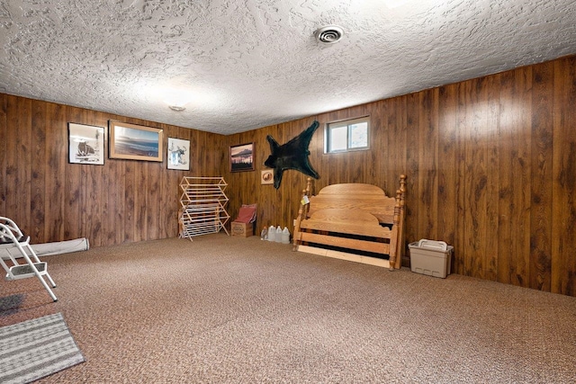 sitting room featuring a textured ceiling, wood walls, carpet flooring, and visible vents