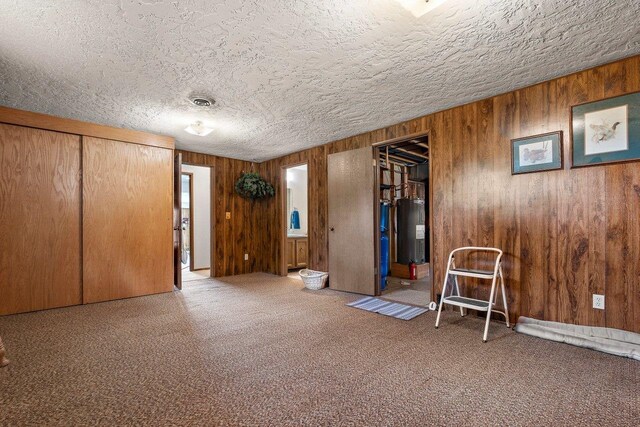 unfurnished bedroom featuring water heater, a textured ceiling, wooden walls, and carpet