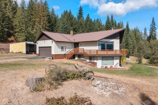 back of property with a lawn, metal roof, a wooded view, a garage, and driveway