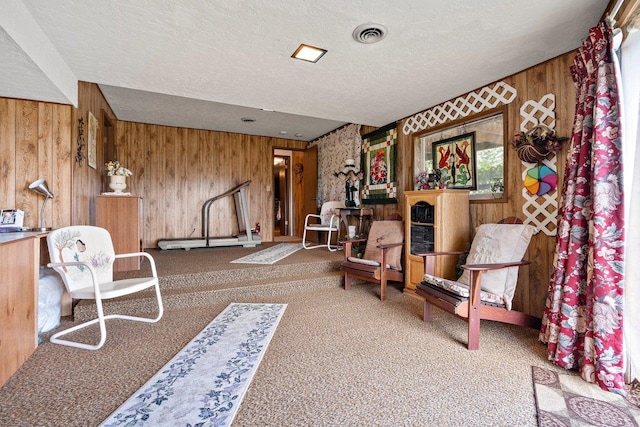 living area featuring carpet flooring, visible vents, a textured ceiling, and wooden walls