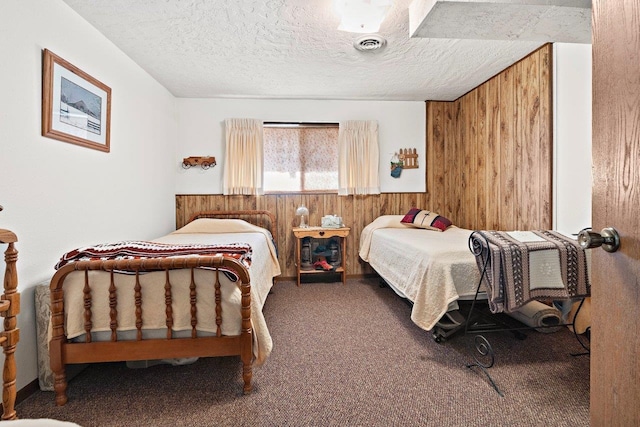 bedroom featuring a textured ceiling, carpet floors, wood walls, wainscoting, and visible vents