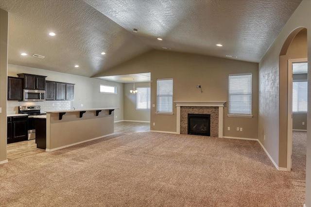 carpeted living room featuring a textured ceiling, lofted ceiling, and a tiled fireplace