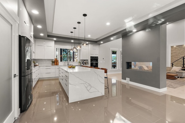 kitchen with sink, white cabinetry, a kitchen island, decorative backsplash, and black appliances