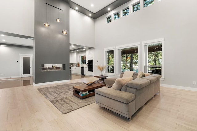 living room featuring plenty of natural light, a towering ceiling, and light hardwood / wood-style flooring